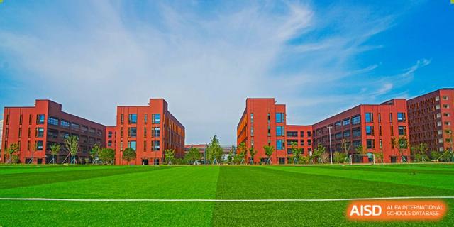 An exterior view of the red brick buildings and sports field at Shanghai United International School Hefei Campus.