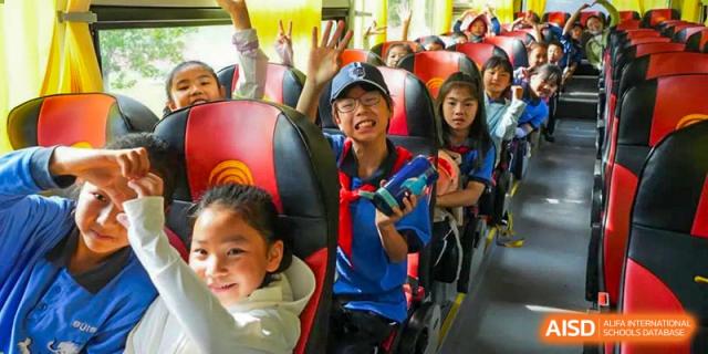A group of students from Shanghai United International School Hefei Campus waving and smiling on a school trip bus.