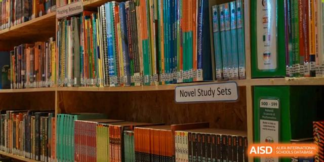 A close-up view of a bookshelf labeled "Novel Study Sets" in the library at Beanstalk International Bilingual School Kunming, showing a variety of books.