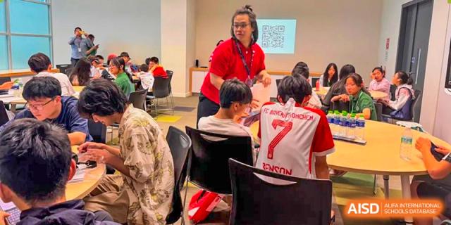 A teacher in a red shirt interacting with students who are seated at tables in a classroom at Beanstalk International Bilingual School Kunming.