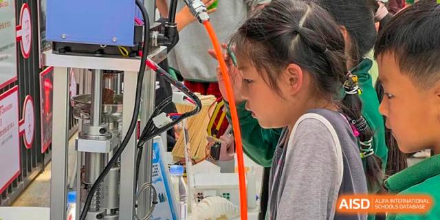 A female student from Beanstalk International Bilingual School Kunming working on a hands-on science or technology project, surrounded by wires and equipment.