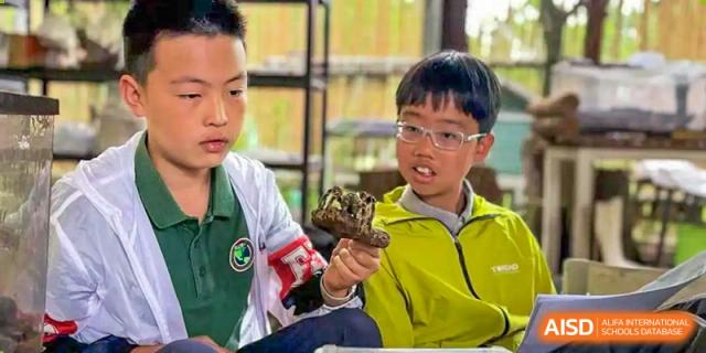 A male student from Beanstalk International Bilingual School Kunming wearing glasses and a yellow jacket, holding a small, unusual object.