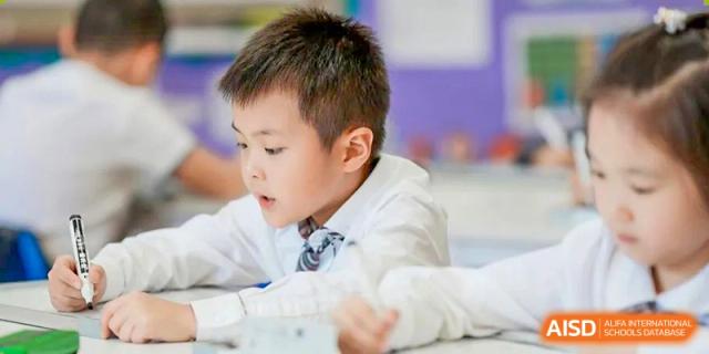 A close-up of a young male student from Beanstalk International Bilingual School Kunming wearing a white shirt and tie, concentrating intently in a classroom setting.