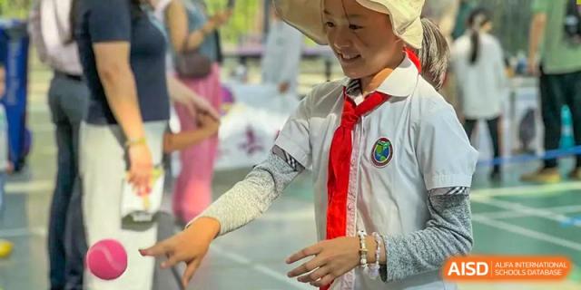 A smiling female student from Beanstalk International Bilingual School Kunming wearing a white shirt and red scarf as part of her uniform, outdoors.