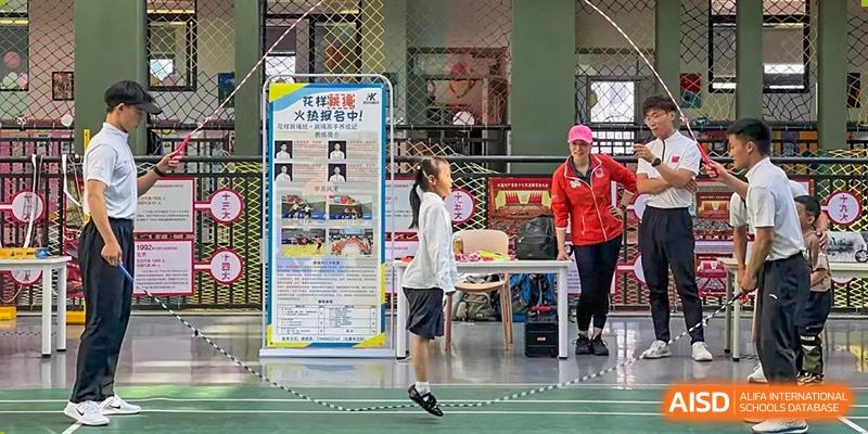 A female student from Beanstalk International Bilingual School Kunming demonstrating rope skipping in front of a display board inside a gym.