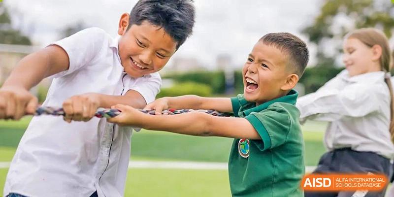 Two young male students from Beanstalk International Bilingual School Kunming laughing joyfully while participating in a team-building activity like tug-of-war.