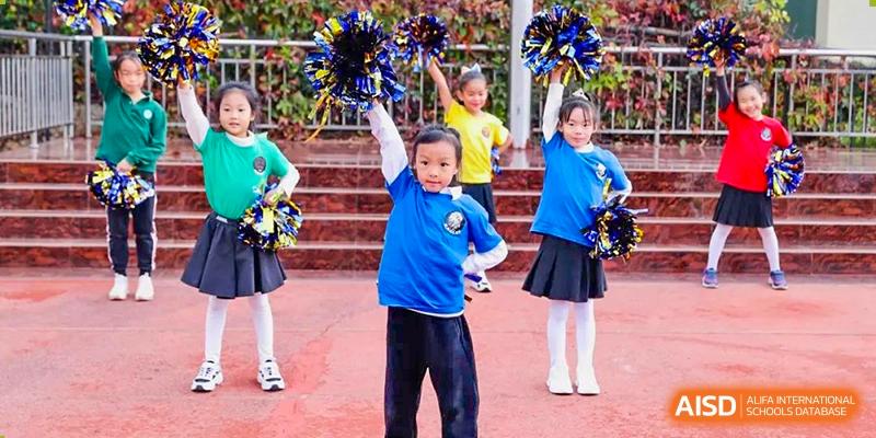 Young students from Beanstalk International Bilingual School Kunming performing a cheerleading or pom-pom dance routine in a group.