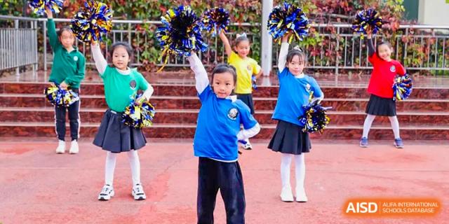 Young students from Beanstalk International Bilingual School Kunming performing a cheerleading or pom-pom dance routine in a group.