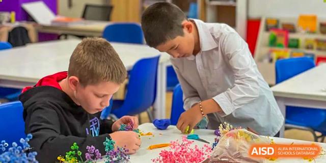 Two male students from Beanstalk International Bilingual School Kunming working together on a colorful craft project with dried flowers and materials on a table.