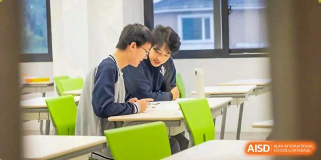 Two male students from Adcote School Shanghai are seated at a desk, smiling while they look at a notebook together.