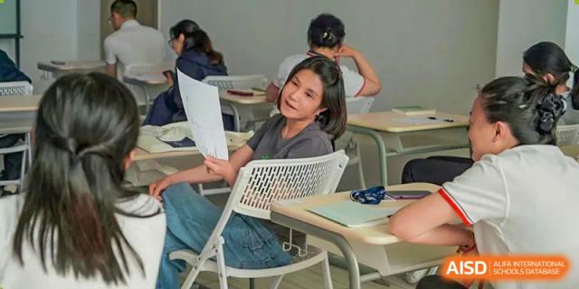 A female student from Adcote School Shanghai is smiling and looking over her shoulder at another student during a class.
