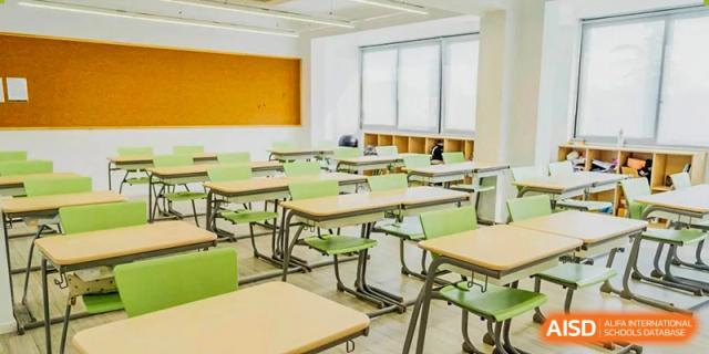 An empty classroom with desks and chairs at Adcote School Shanghai, with natural light coming in from the window.