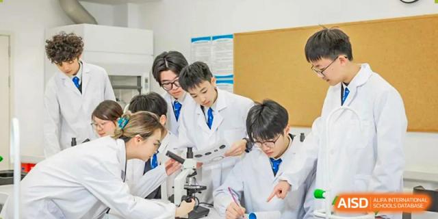 A group of students from Adcote School Shanghai are in a science lab, wearing lab coats and using microscopes for an experiment.