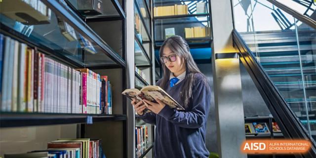 A female student from Adcote School Shanghai is looking through books on a shelf in the school's library.