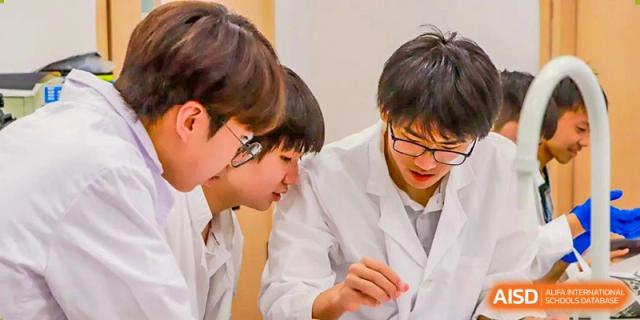 Two male students from Adcote School Shanghai are wearing lab coats and safety goggles while working on a science project together.