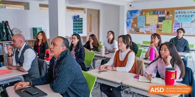 A group of students from Adcote School Shanghai are seated at tables in a classroom, listening to a lecture or presentation.
