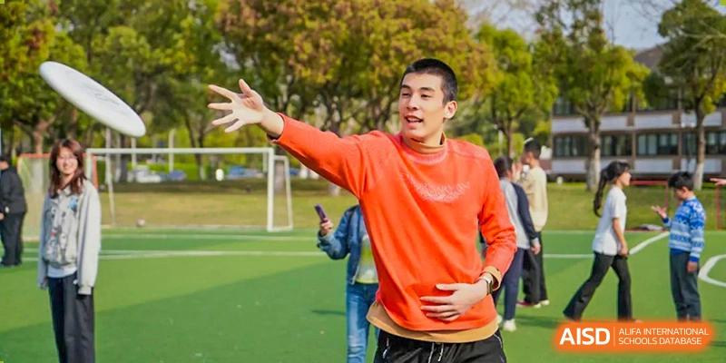A male student in an orange sweater from Adcote School Shanghai is enthusiastically participating in an outdoor sports activity.