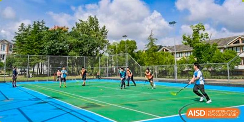 A group of students from Adcote School Shanghai are playing field hockey on an outdoor green and blue sports court.