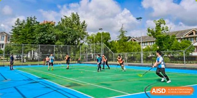 A group of students from Adcote School Shanghai are playing field hockey on an outdoor green and blue sports court.