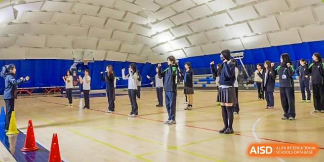 Students from Adcote School Shanghai are participating in a group exercise or dance session inside a gymnasium.