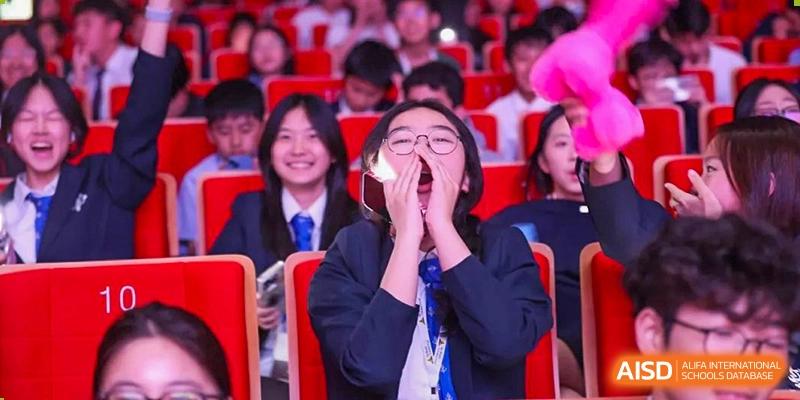 A female student from Adcote School Shanghai smiles and cheers enthusiastically while wearing a school uniform.