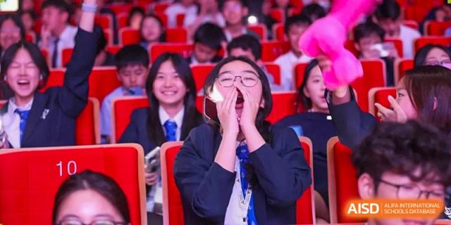 A female student from Adcote School Shanghai smiles and cheers enthusiastically while wearing a school uniform.