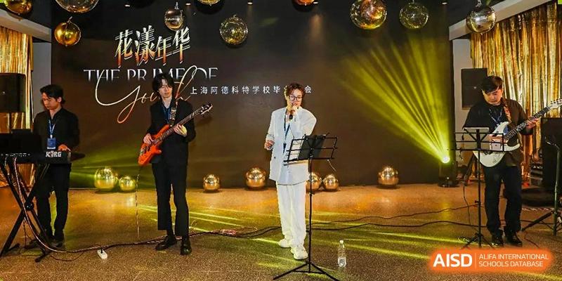 A male student from Adcote School Shanghai performs on a stage, singing into a microphone with a band behind him.