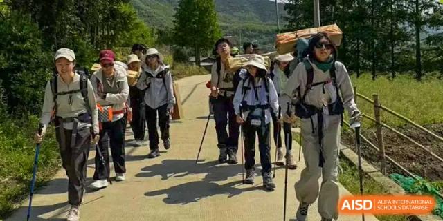 A group of students and teachers from Adcote School Shanghai are hiking on a dirt path under the sun.