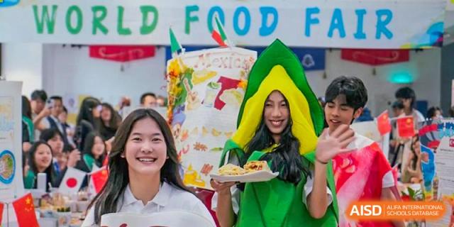 Two students, one dressed as a cartoon avocado, from Adcote School Shanghai smile and hold up a plate of food at a school event.