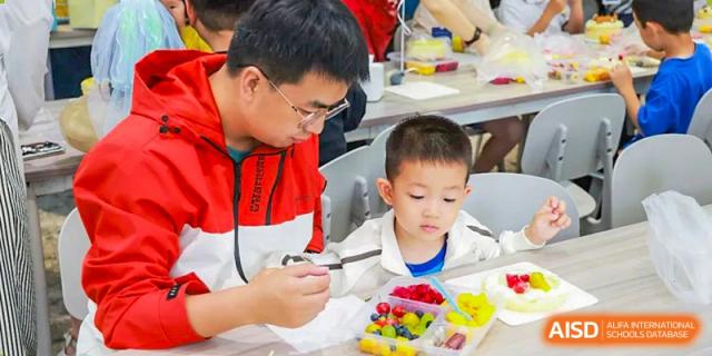 A teacher from Adcote School Shanghai helps a young student prepare food in a cooking class.