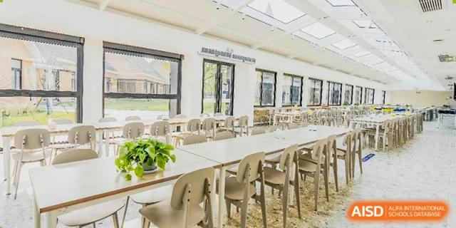 The school cafeteria or dining hall at Adcote School Shanghai with white tables and chairs and an outdoor patio.