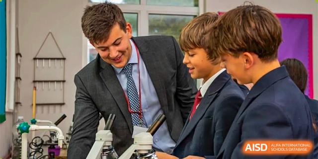 A teacher in a suit and tie working with two male students at a microscope in a science lab at Bromsgrove School Mission Hills.
