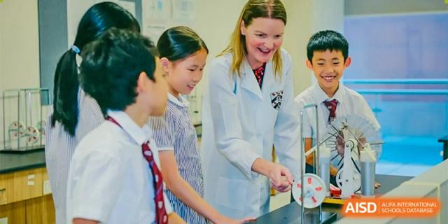 A teacher in a white lab coat helping two female students with a science experiment at Bromsgrove School Mission Hills.