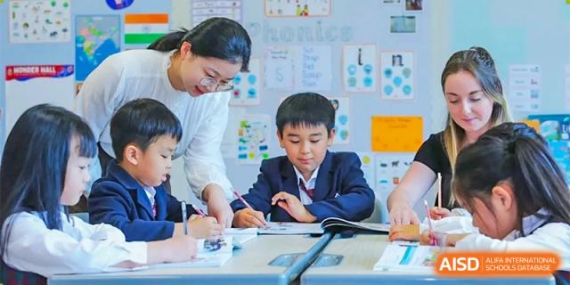 A teacher sitting at a table and helping a male student with his writing at Bromsgrove School Mission Hills.