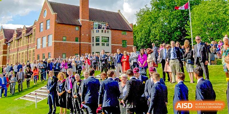 A large group of people, including students, teachers, and parents, gathered outside a brick building at Bromsgrove School Mission Hills.