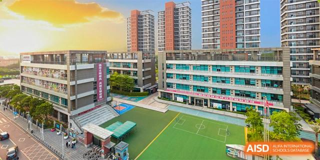 An aerial view of the Bromsgrove School Mission Hills campus, showing a sports field and modern apartment buildings under a bright sky.