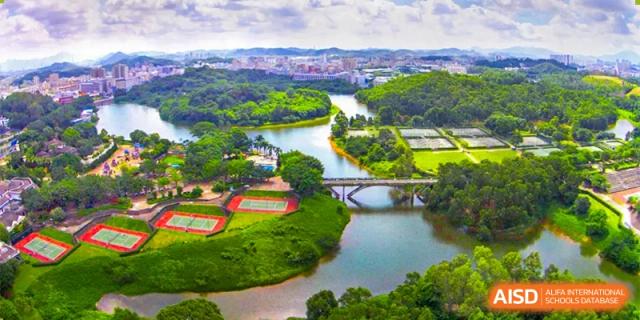An aerial view of the Bromsgrove School Mission Hills campus, showing a river, sports fields, and lush greenery surrounded by a city skyline.