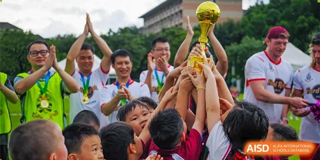 A group of students and a coach celebrating a victory, raising a golden trophy in the air at Bromsgrove School Mission Hills.
