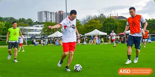A student in a red and white jersey dribbling a soccer ball on a green field during a sports event at Bromsgrove School Mission Hills.