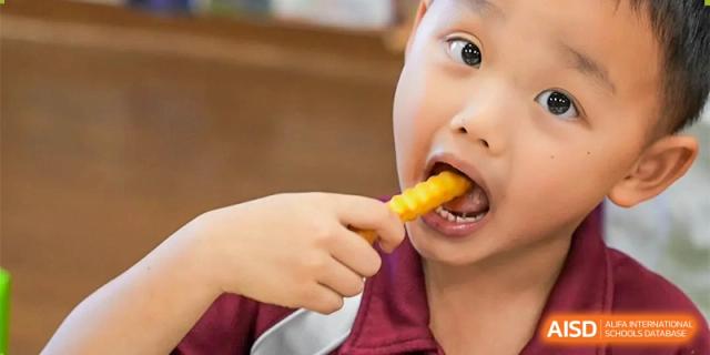 A young student at Bromsgrove School Mission Hills eating a french fry, seen in a close-up shot.