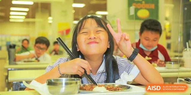 A female student at Bromsgrove School Mission Hills smiling and giving a peace sign while eating a meal.