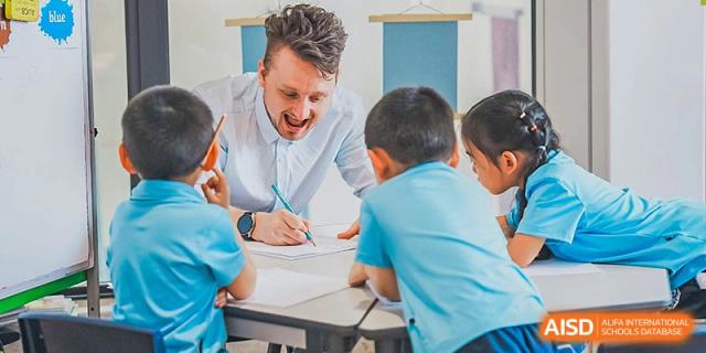 A teacher smiling while helping young Harrow Lide High School Nanning students with a writing activity in a classroom.