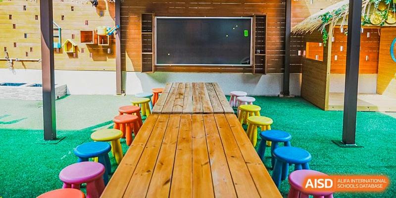 Harrow Lide High School Nanning outdoor classroom setup with a long wooden table, colorful stools, and a large blackboard.