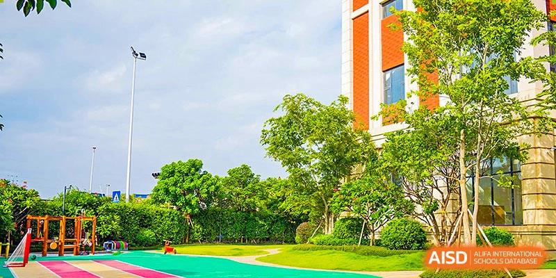 Lush green lawn and trees in the spacious outdoor area of Harrow Lide High School Nanning with bright school buildings in the background.