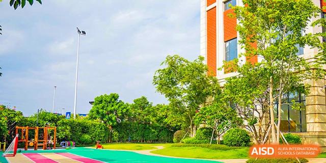 Lush green lawn and trees in the spacious outdoor area of Harrow Lide High School Nanning with bright school buildings in the background.