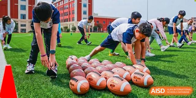 Harrow Lide High School Nanning students participating in an outdoor sports session, focusing on a pile of American footballs on the grass.