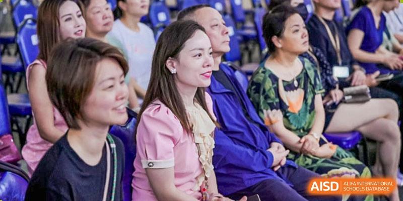 Spectators, including a woman in a pink top, watching an event in the stands at Harrow Lide High School Nanning.
