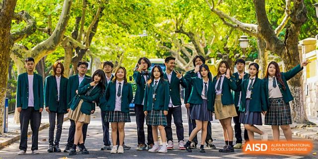 A large group of students in their uniform stand together outdoors under trees, posing for a photo at Guokai International School of Qingdao.