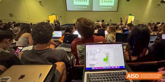 A student is working on a laptop in a classroom or lecture hall setting at Guokai International School of Qingdao.