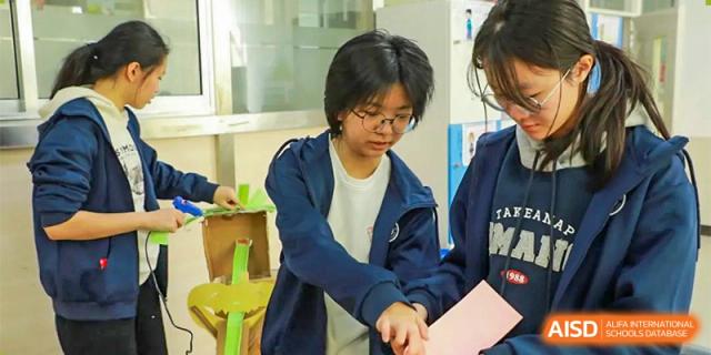 A close-up of a female student in a dark blue jacket working on a collaborative project with others at Guokai International School of Qingdao.